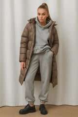 Women's long brown padded winter coat styled with gray hoodie and joggers